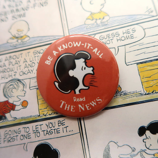 White, red and black large vintage can badge featuring beloved character Lucy van Pelt from the Snoopy/Peanuts comics yelling "Be a know-it-all, read the news" in white lettering!   